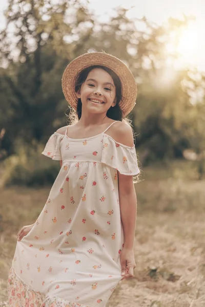 Pretty young girl model on sunset in park wearing in sundress and hat. Portrait of beautiful child in park in summer