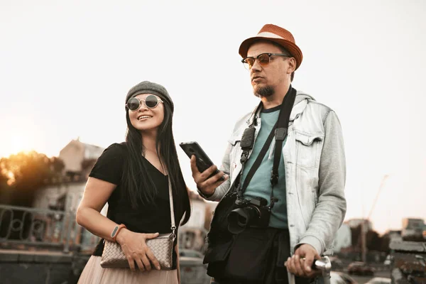 Handsome couple on street. Urban stylish two people walking on city background. Handsome man in denim jacket, hat and sunglasses. Attractive woman in casual shirt and skirt