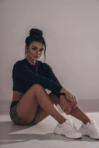 Çekici bir portre. Esmer saçlı, iç çamaşırlı, beyaz arka planda spor ayakkabılı seksi bir kız.