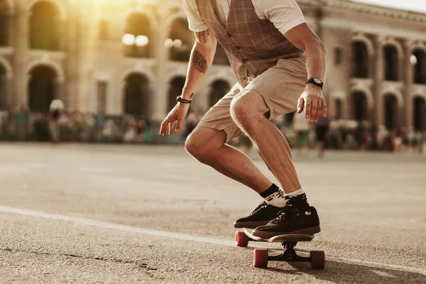 都会人の生活 スタイリッシュな男は街の通りに白いシャツでスケートボードに乗る 建物の背景に道路の近くにハンサムなひげそりのヒップスター男性の肖像画 — ストック写真