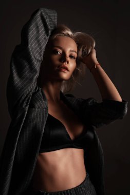 Portrait of elegant attractive girl in underwear and suit. Sexy fashion style woman model posing on black background