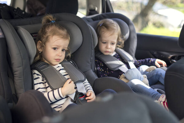 cute small twins in gray car seats in the car