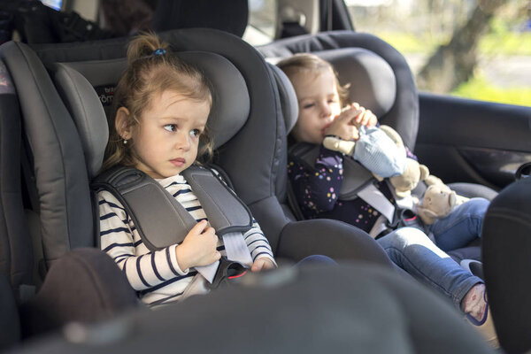 cute small twins in gray car seats in the car