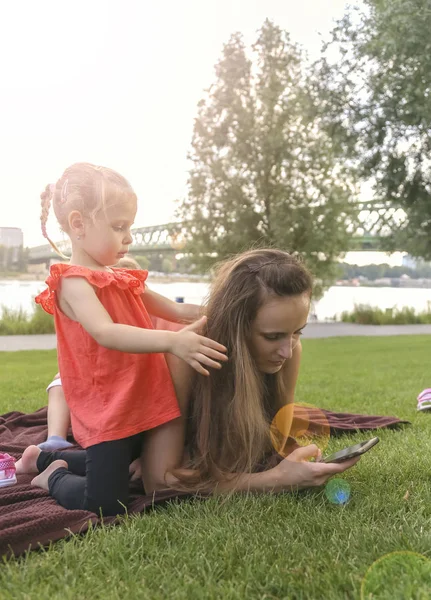 Μητέρα με κόρες που κάνουν πικ-νικ δίπλα στο ποτάμι, μιλάει στο smartphone — Φωτογραφία Αρχείου