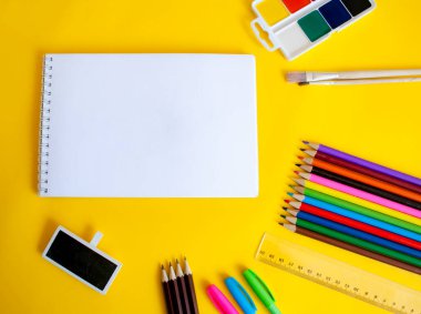 boş sayfalı defter, renkli kalemler, kalemler, boyalar, cetvel ve fırçalar sarı arkaplan görünümünde
