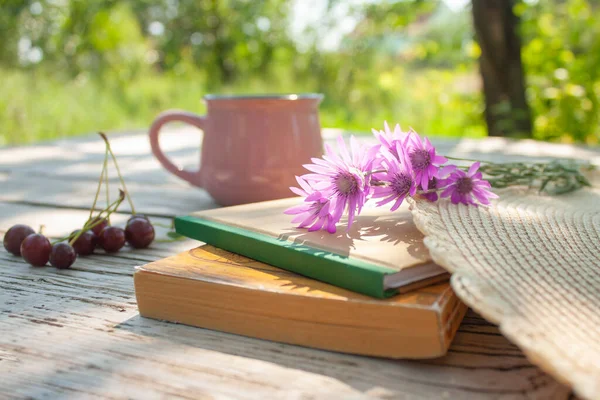 closed books, flowers, cherry berries and a cup on a table in the garden