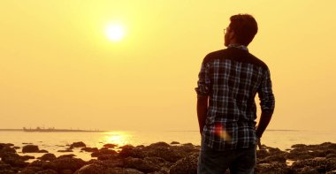 Genç ve mutlu bir adam Mercan Denizi sahilinde günbatımının tadını çıkarıyor. .