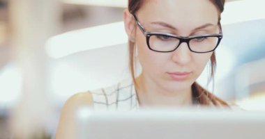 İş kadını portresi laptopta çalışıyor. Ortak Çalışma Alanı 'nda. Yakın çekim. 4K Yavaşlama Hareketi, DCI. Genç iş kadını, gözlük takıyor, modern ofis binasında taşınabilir bilgisayar kullanıyor..