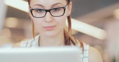 İş kadını portresi laptopta çalışıyor. Ortak Çalışma Alanı 'nda. Yakın çekim. 4K Yavaşlama Hareketi, DCI. Genç iş kadını, gözlük takıyor, modern ofis binasında taşınabilir bilgisayar kullanıyor..