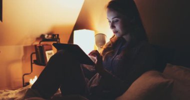Geceleri Tablet Bilgisayar kullanan bir kadın. Yavaş hareket et. 4K DCI. Genç milenyum tüketicisi evden online alışveriş yapıyor, yatakta yatıyor. Günlük yaşamda teknoloji. Doli Vuruşu.