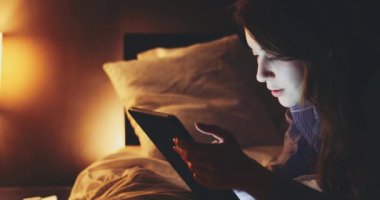 Geceleri Tablet Bilgisayar kullanan bir kadın. Yavaş hareket et. 4K DCI. Genç milenyum tüketicisi evden online alışveriş yapıyor, yatakta yatıyor. Günlük yaşamda teknoloji.