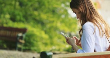 Sunny Park 'ta Akıllı Telefon Kullanan Kadın Rahatlıyor. Yavaş bir hareket yap. Güzel Milenyum Kadını botanik bahçesinde cep telefonuyla fotoğraf çekiyor..