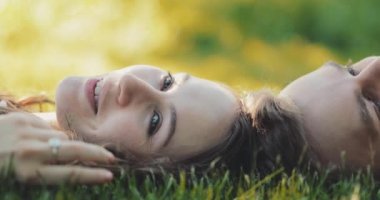 Yeşil Çimlerde Rahatlayan Mutlu Çift, Top View. Yavaş haraket 4K. Gülümseyen adam ve aşık kadın yaz tatilinin tadını çıkarıyorlar. Neşeli bir aile. Genç aşıklar çimenlerde uzanıyor, dışarıda dinleniyorlar..