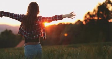 Gün batımında açık havada dans eden çekici genç bir kadın silueti. Arkasında parlak bir güneş var. Yavaş çekim