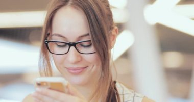 İş kadını portresi. Ortak Çalışma Alanında Akıllı Telefon Kullanıyor. Yakın plan. 4K Yavaşlama Hareketi, DCI. Genç iş kadını, gözlük takıyor, modern ofis binasında cep telefonu kullanıyor..