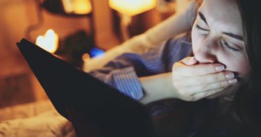 Geceleri Tablet Bilgisayar kullanan bir kadın. Yavaş hareket et. 4K DCI. Genç milenyum tüketicisi evden online alışveriş yapıyor, yatakta yatıyor. Günlük yaşamda teknoloji.