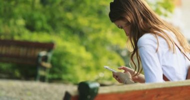 Sunny Park 'ta Akıllı Telefon Kullanan Kadın Rahatlıyor. Yavaş bir hareket yap. Güzel Milenyum Kadını botanik bahçesinde cep telefonuyla fotoğraf çekiyor..