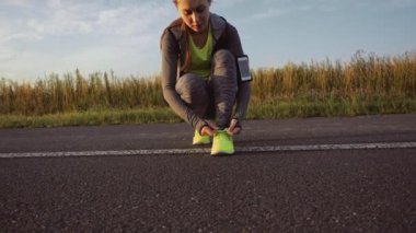 Sonbahar yollarında koşu ayakkabılarıyla koşmak için bağcıklarını bağlayan bayan sporcu. Koşucu antrenmana hazırlanıyor. Spor yaşam tarzı. Yavaş çekim.