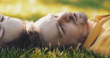 Yeşil Çimlerde Rahatlayan Mutlu Çift, Top View. Yavaş haraket 4K. Gülümseyen adam ve aşık kadın yaz tatilinin tadını çıkarıyorlar. Neşeli bir aile. Genç aşıklar çimenlerde uzanıyor, dışarıda dinleniyorlar..