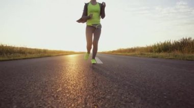 Koşucu kadın dışarıda koşuyor. Güneşli yolda antrenman yaparken çıplak ayaklı spor ayakkabısı giyen bir kadın. Ağır çekim. Mercek Fişeği