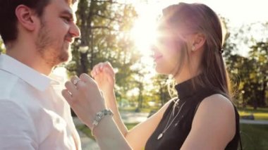 Genç mutlu çift şehir parkında sarılıp öpüşüyor. Yavaş bir hareket yap. Güzel romantik erkek ve kadın gün batımında bir aşk öpücüğü paylaşıyor..