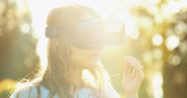 Sanal Gerçeklik Gözlüklü Kadın Tezahürat Yapıyor. Yavaş haraket 4K. Sanal 3 boyutlu dünyanın tadını çıkaran, VR kulaklıkla oynayan neşeli genç bir kadın. Güneşli alan arkaplanı, hayali gerçekliğin içinde.