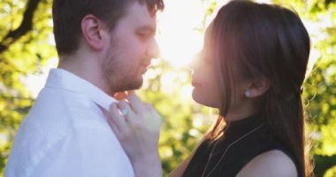 Şehir parkında sarılıp öpüşen genç çift. 4K Yavaşlama Hareketi. Güzel romantik erkek ve kadın gün batımında öpüşürler..