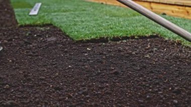 Bahçıvan bir tırmıkla toprağı temizliyor. Yavaş bir hareket yap. Tanımlanamayan insanların elleri toprağı düzleştiriyor, mükemmel çimler dikiyor, yeşil çimenler dikiyor. Manzara tasarımı üzerinde çalışan bir adam..