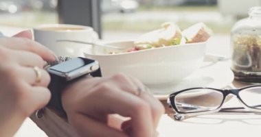 Pencere kenarındaki bir kafede Akıllı Saat Kullanan Kadın Eller, Yaklaş. 4K Yavaşlama Hareketi, DCI. Genç iş kadını elleri, öğle yemeği sırasında modern barda ukalalık yapıyor. Hayatta Teknoloji