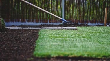 Bahçıvan bir tırmıkla toprağı temizliyor. Yavaş bir hareket yap. Tanımlanamayan insanların elleri toprağı düzleştiriyor, mükemmel çimler dikiyor, yeşil çimenler dikiyor. Manzara tasarımı üzerinde çalışan bir adam..