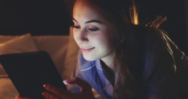 Geceleri Tablet Bilgisayar kullanan bir kadın. Yavaş hareket et. 4K DCI. Genç milenyum tüketicisi evden online alışveriş yapıyor, yatakta yatıyor. Günlük yaşamda teknoloji.