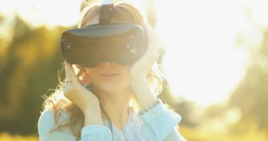 Sanal Gerçeklik Gözlüklü Kadın Tezahürat Yapıyor. Yavaş haraket 4K. Sanal 3 boyutlu dünyanın tadını çıkaran, VR kulaklıkla oynayan neşeli genç bir kadın. Güneşli alan arkaplanı, hayali gerçekliğin içinde.