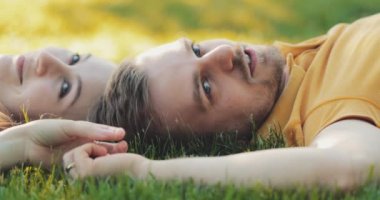 Yeşil Çimlerde Rahatlayan Mutlu Çift, Top View. Yavaş haraket 4K. Gülümseyen adam ve aşık kadın yaz tatilinin tadını çıkarıyorlar. Neşeli bir aile. Genç aşıklar çimenlerde uzanıyor, dışarıda dinleniyorlar..