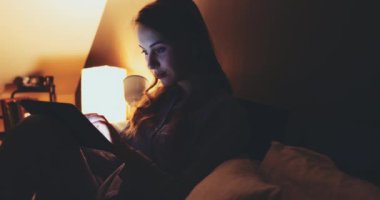 Geceleri Tablet Bilgisayar kullanan bir kadın. Yavaş hareket et. 4K DCI. Genç milenyum tüketicisi evden online alışveriş yapıyor, yatakta yatıyor. Günlük yaşamda teknoloji. Doli Vuruşu.