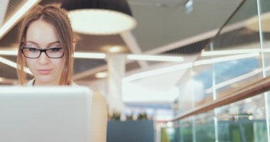 İş kadını portresi birlikte çalışma alanında dizüstü bilgisayarda çalışıyor. 4K Yavaşlama Hareketi, DCI. Genç bir iş kadını, gözlük takıyor, modern ofis binasında taşınabilir bilgisayar kullanıyor. Hayatta Teknoloji