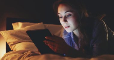 Geceleri Tablet Bilgisayar kullanan bir kadın. Yavaş hareket et. 4K DCI. Genç milenyum tüketicisi evden online alışveriş yapıyor, yatakta yatıyor. Günlük yaşamda teknoloji.