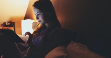 Geceleri Tablet Bilgisayar kullanan bir kadın. Yavaş hareket et. 4K DCI. Genç milenyum tüketicisi evden online alışveriş yapıyor, yatakta yatıyor. Günlük yaşamda teknoloji. Doli Vuruşu.