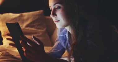 Geceleri Tablet Bilgisayar kullanan bir kadın. Yavaş hareket et. 4K DCI. Genç milenyum tüketicisi evden online alışveriş yapıyor, yatakta yatıyor. Günlük yaşamda teknoloji.