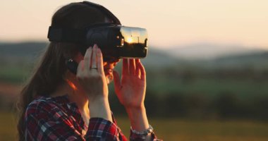 Sanal Gerçeklik Gözlüklü Kadın Tezahürat Yapıyor. Yavaş haraket 4K. Sanal 3 boyutlu dünyanın tadını çıkaran, VR kulaklıkla oynayan neşeli genç bir kadın. Güneşli alan arkaplanı, hayali gerçekliğin içinde.