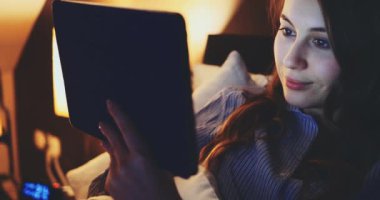 Geceleri Tablet Bilgisayar kullanan bir kadın. Yavaş hareket et. 4K DCI. Genç milenyum tüketicisi evden online alışveriş yapıyor, yatakta yatıyor. Günlük yaşamda teknoloji.