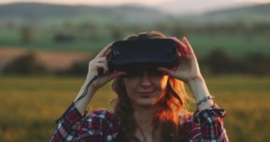 Sanal Gerçeklik Gözlüklü Kadın Tezahürat Yapıyor. Yavaş haraket 4K. Sanal 3 boyutlu dünyanın tadını çıkaran, VR kulaklıkla oynayan neşeli genç bir kadın. Güneşli alan arkaplanı, hayali gerçekliğin içinde.