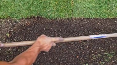 Bahçıvan bir tırmıkla toprağı temizliyor. Yavaş bir hareket yap. Tanımlanamayan insanların elleri toprağı düzleştiriyor, mükemmel çimler dikiyor, yeşil çimenler dikiyor. Manzara tasarımı üzerinde çalışan bir adam..