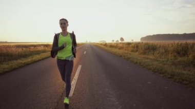 Koşucu kadın dışarıda koşuyor. Güneşli yolda antrenman yaparken çıplak ayaklı spor ayakkabısı giyen bir kadın. Ağır çekim. Mercek Fişeği