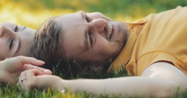 Yeşil Çimlerde Rahatlayan Mutlu Çift, Top View. Yavaş haraket 4K. Gülümseyen adam ve aşık kadın yaz tatilinin tadını çıkarıyorlar. Neşeli bir aile. Genç aşıklar çimenlerde uzanıyor, dışarıda dinleniyorlar..