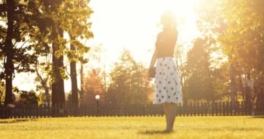 Şehir parkında el ele tutuşup sohbet eden genç mutlu çift. 4K DCI Yavaş Hareketi. Güzel, romantik, gülümseyen bir kadın ve bir erkek gün batımında kameraya doğru yürüyorlar.