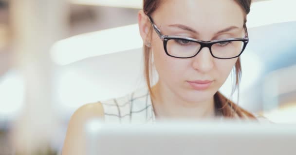Portrét podnikatelky pracující na notebooku ve spolupracujícím prostoru, zblízka. 4K SLOW MOTION, DCi. Mladá podnikatelka, nosí brýle, používá přenosný počítač v moderní kancelářské budově. — Stock video