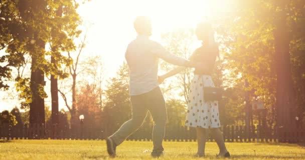 若い幸せなカップルが街の公園で散歩し 手を取り合って話しています Dciスローモーション 美しいロマンチックな笑顔の男と女性がお互いを楽しんで 夕日の屋外でカメラに歩いて — ストック動画