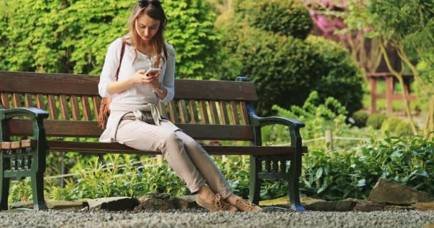 Een Vrouw Die Smartphone Relaxes Gebruikt Sunny Park Vertraag Bewegen — Stockvideo