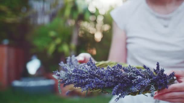 女人做薰衣草花环 缓慢的运动 无法辨认的女花匠手用紫色薰衣草花做装饰 女孩在普罗旺斯法国花园享受宁静的夜晚 — 图库视频影像