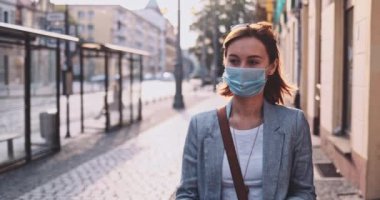 Şehirde koruyucu maske takan, akıllı telefon kullanan bir kadın var. Yavaş hareket, Gimbal Dengeleyici. Hava kirliliği ve Coronavirus Covid-19 'a karşı maskeli genç bir kadın. Şehir Sabahı.